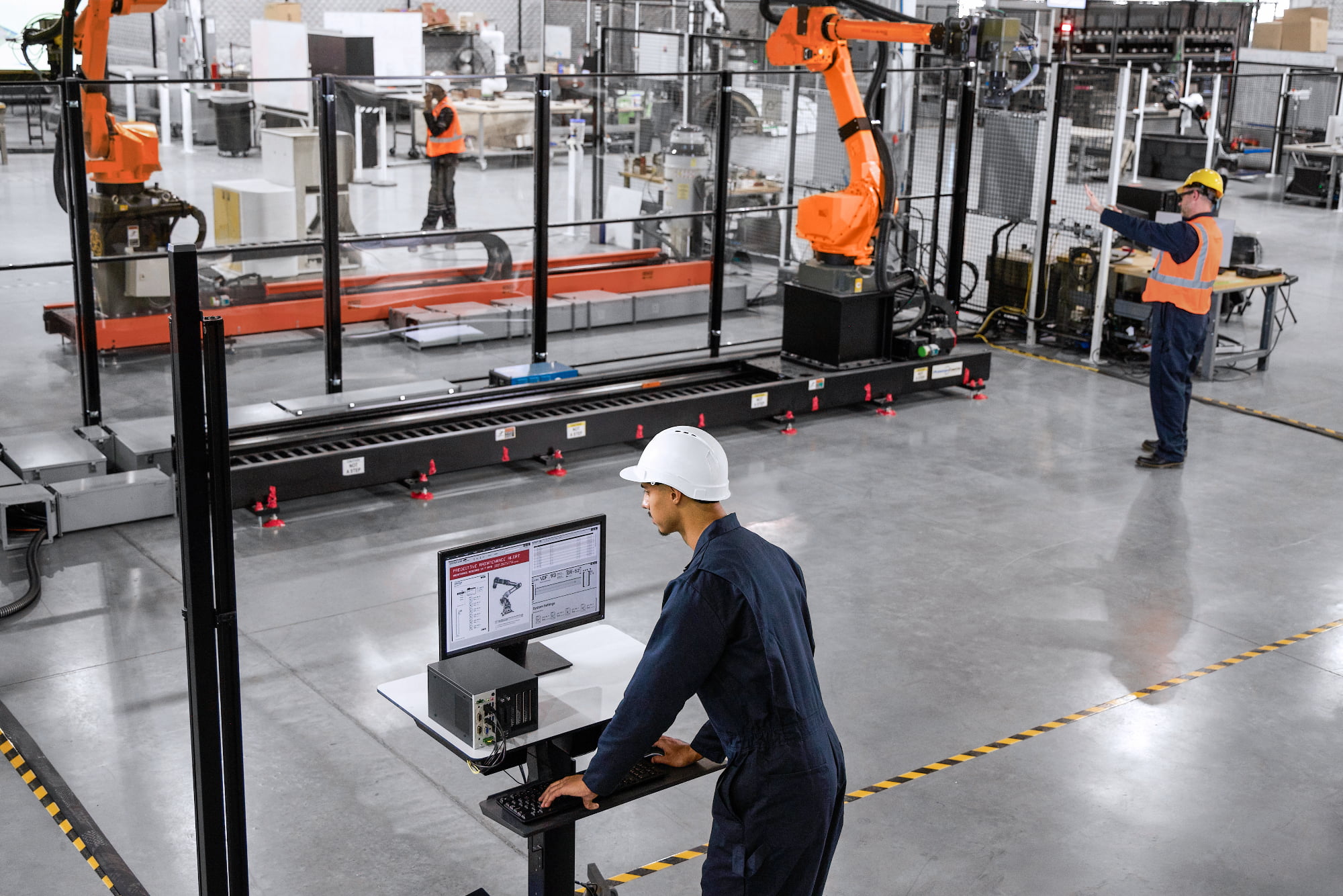 A technician monitors predictive maintenance alerts on a factory floor as an industrial robotic arm operates nearby.